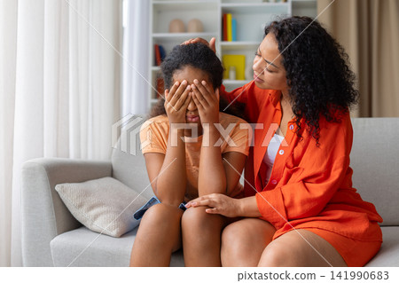 Concerned Black mother comforting her upset young daughter covering her face Concerned Black mother comforting her upset young daughter covering her face 141990683