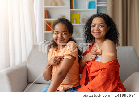 Smiling black mother and daughter both showing bandaged arms after vaccination Smiling black mother and daughter both showing bandaged arms after vaccination 141990684