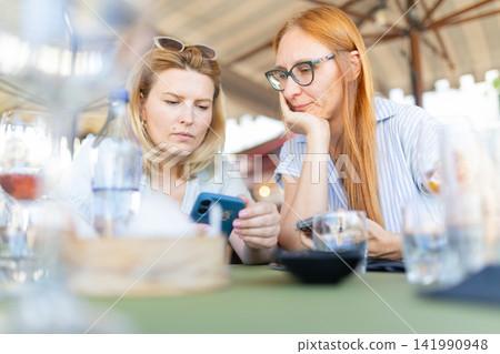 Women concentrating on smartphone screens at outdoor restaurant Women concentrating on smartphone screens at outdoor restaurant 141990948