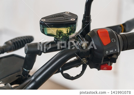 Close up of motorcycle handlebar controls and brake fluid reservoir with red switches on black metal frame. Close up of motorcycle handlebar controls and brake fluid reservoir with red switches on black metal frame. 141991078