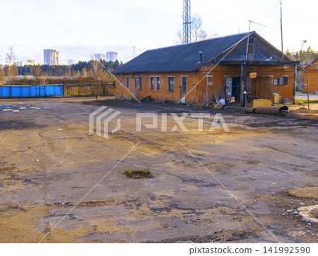 Single-story brick industrial building beside cracked asphalt lot under pale sky Single-story brick industrial building beside cracked asphalt lot under pale sky 141992590