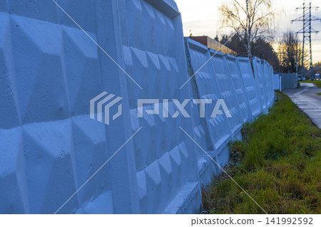 Painted concrete fence panels lining suburban roadside with textured geometric surface at dusk Painted concrete fence panels lining suburban roadside with textured geometric surface at dusk 141992592