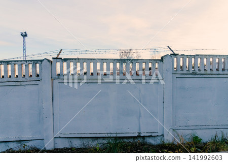 Weathered concrete perimeter wall topped with barbed wire under pastel evening sky Weathered concrete perimeter wall topped with barbed wire under pastel evening sky 141992603