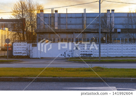 Industrial warehouse building behind concrete perimeter wall at dusk with empty street Industrial warehouse building behind concrete perimeter wall at dusk with empty street 141992604