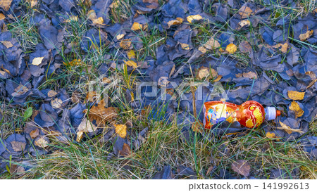 Discarded plastic beverage bottle lying on damp autumn grass with fallen leaves and muted natural textures Discarded plastic beverage bottle lying on damp autumn grass with fallen leaves and muted natural textures 141992613