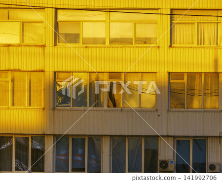 Sunlit yellow industrial building facade with reflective windows and corrugated panels Sunlit yellow industrial building facade with reflective windows and corrugated panels 141992706