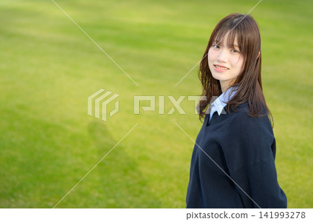 一名日本高中女生轉身,在草地上微笑。 一名日本高中女生轉身,在草地上微笑。 141993278