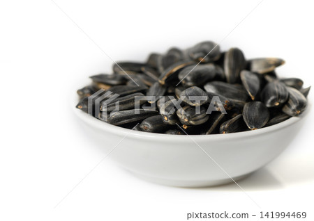 Close-Up Side View of a Small White Bowl Filled with Whole Black Sunflower Seeds Close-Up Side View of a Small White Bowl Filled with Whole Black Sunflower Seeds 141994469