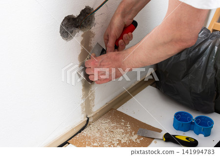 A person smooths plaster onto a white apartment wall, carefully applying it around a hole where an electrical outlet will be installed A person smooths plaster onto a white apartment wall, carefully applying it around a hole where an electrical outlet will be installed 141994783