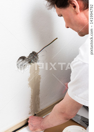 A person smooths plaster onto a white apartment wall, carefully applying it around a hole where an electrical outlet will be installed A person smooths plaster onto a white apartment wall, carefully applying it around a hole where an electrical outlet will be installed 141994792