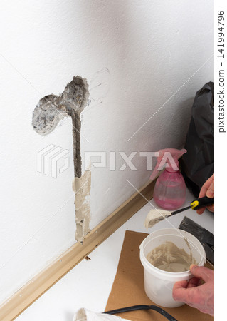 Hands are shown thoroughly mixing plaster in a white bucket with two spatulas, ready to repair an apartment wall Hands are shown thoroughly mixing plaster in a white bucket with two spatulas, ready to repair an apartment wall 141994796