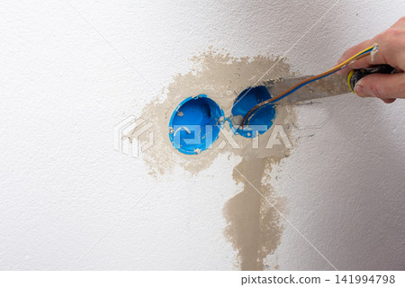 A person smooths plaster onto a white apartment wall, carefully applying it around a hole where an electrical outlet will be installed A person smooths plaster onto a white apartment wall, carefully applying it around a hole where an electrical outlet will be installed 141994798
