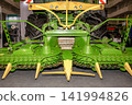 Green farm equipment displayed at an agricultural event in a large exhibition room with many visitors 141994826