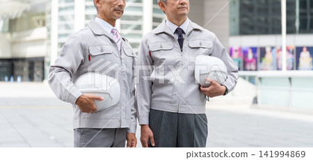 Senior man in work clothes holding a helmet Senior man in work clothes holding a helmet 141994869