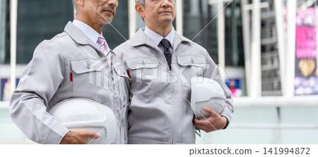 Senior man in work clothes holding a helmet Senior man in work clothes holding a helmet 141994872