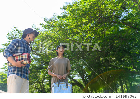 A young man and woman enjoying camping in the dappled sunlight filtering through the trees. A young man and woman enjoying camping in the dappled sunlight filtering through the trees. 141995062