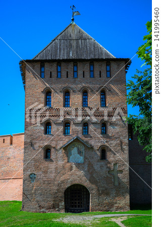 Ancient stone tower stands tall against clear blue sky. Weathered brick walls show signs of age and history. Dark arched doorway invites viewers into its past Ancient stone tower stands tall against clear blue sky. Weathered brick walls show signs of age and history. Dark arched doorway invites viewers into its past 141995460