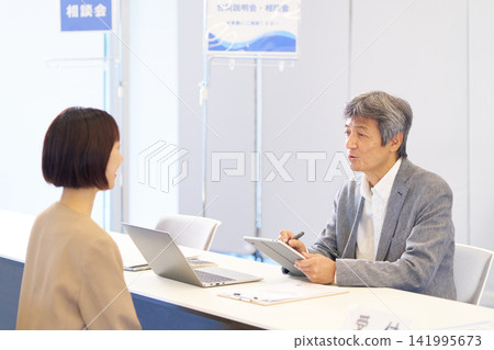 資深男性諮商師和一位女訪客在諮商過程中使用平板電腦進行解說。 資深男性諮商師和一位女訪客在諮商過程中使用平板電腦進行解說。 141995673