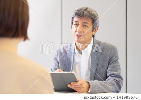 一位資深男性顧問一邊拿著平板電腦一邊冷靜地解釋。 141995676