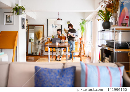 Women gathered around laptops and documents in the living room. Women gathered around laptops and documents in the living room. 141996160