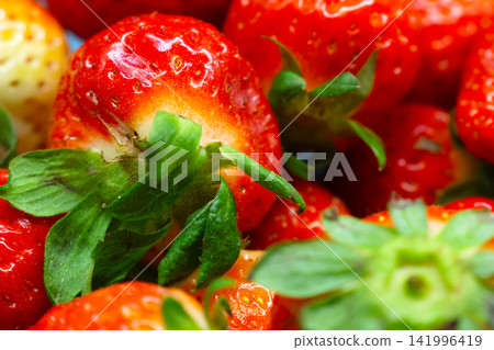 Fresh red strawberries with green leaves arranged closely, showcasing their vibrant color and texture against a blurred background Fresh red strawberries with green leaves arranged closely, showcasing their vibrant color and texture against a blurred background 141996419