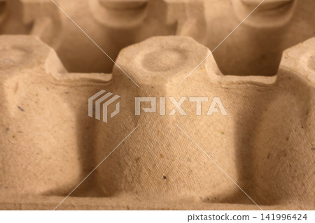 Close-up view of a brown recycled paper egg carton with individual compartments designed for holding eggs, showcasing texture and material details Close-up view of a brown recycled paper egg carton with individual compartments designed for holding eggs, showcasing texture and material details 141996424