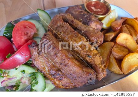 Delicious Grilled Pork Ribs with Fresh Salad and Potato Wedges on a Rustic Platter Delicious Grilled Pork Ribs with Fresh Salad and Potato Wedges on a Rustic Platter 141996557