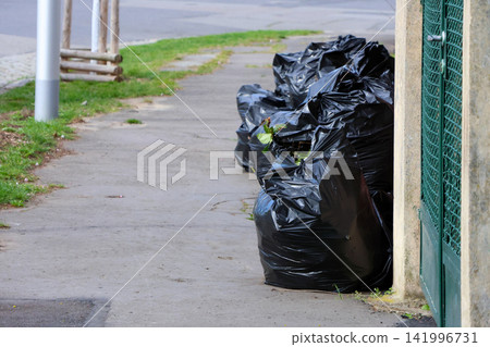Urban Cleanup: Pile of Garbage Bags on City Sidewalk for Waste Management Awareness 141996731