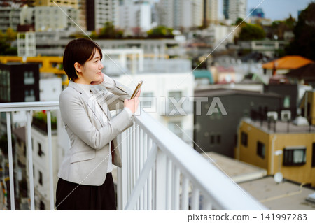 一位女商人站在城市陽台上看著她的智慧型手機。 一位女商人站在城市陽台上看著她的智慧型手機。 141997283