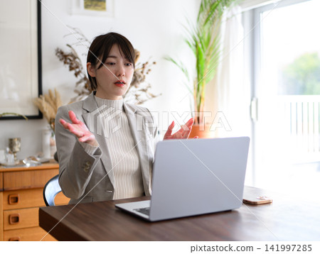 A Japanese woman in her 20s explains during an online meeting using her laptop. A Japanese woman in her 20s explains during an online meeting using her laptop. 141997285
