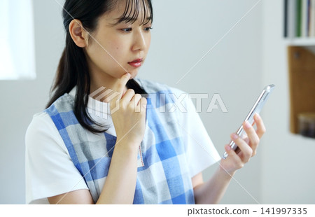 Kitchen - Image of a woman thinking up recipes on her smartphone. Kitchen - Image of a woman thinking up recipes on her smartphone. 141997335
