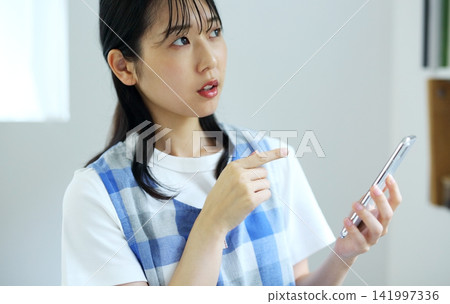 廚房-一位女士正在用智慧手機構思菜譜的圖片。 廚房-一位女士正在用智慧手機構思菜譜的圖片。 141997336