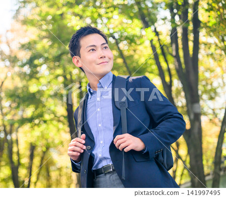 A man with a backpack on looks up at the sky in a park bathed in dappled sunlight. A man with a backpack on looks up at the sky in a park bathed in dappled sunlight. 141997495