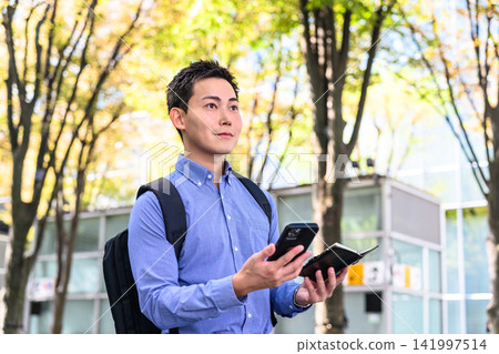 一名男子拿著智慧型手機和筆記本走在街上。 一名男子拿著智慧型手機和筆記本走在街上。 141997514