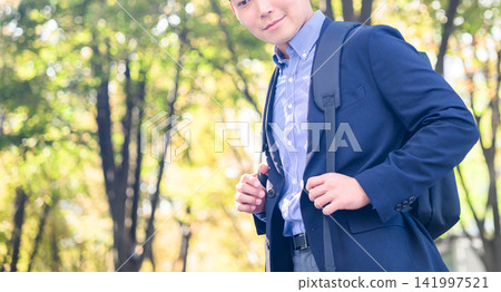 A man is wearing a backpack and is adjusting his jacket with a relaxed expression. A man is wearing a backpack and is adjusting his jacket with a relaxed expression. 141997521