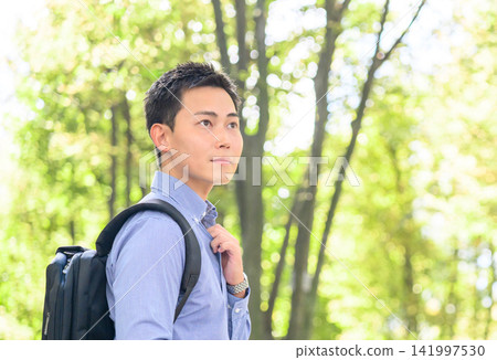 A man walking in the dappled sunlight with a backpack on. A man walking in the dappled sunlight with a backpack on. 141997530