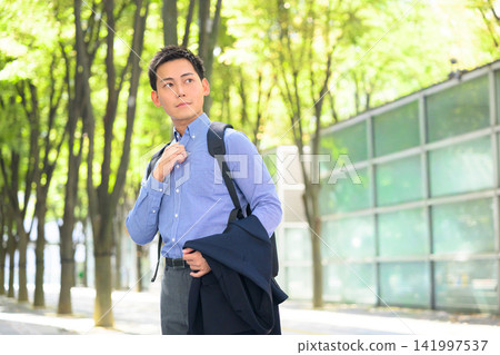 一名男子沿著綠樹成蔭的街道行走,陽光透過樹葉灑下斑駁的光影。 一名男子沿著綠樹成蔭的街道行走,陽光透過樹葉灑下斑駁的光影。 141997537