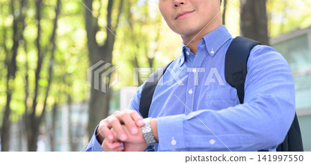 一名男子背著背包，正在檢查手錶。 141997550