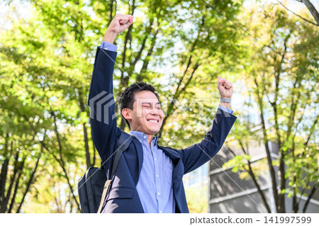 A businessman raising both hands in celebration outdoors. A businessman raising both hands in celebration outdoors. 141997599