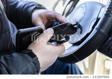 A driver adjusts a smartphone in a suction cup mount on a vehicle dashboard to illustrate modern automotive technology for safe navigation and communication during daily transport A driver adjusts a smartphone in a suction cup mount on a vehicle dashboard to illustrate modern automotive technology for safe navigation and communication during daily transport 141997666