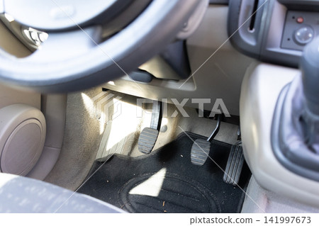 Three foot pedals inside a car cockpit featuring a clutch brake and accelerator for manual transmission driving, conveying the mechanical control and operation of an automotive vehicle Three foot pedals inside a car cockpit featuring a clutch brake and accelerator for manual transmission driving, conveying the mechanical control and operation of an automotive vehicle 141997673