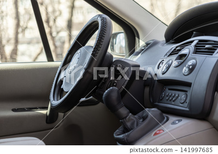 Modern vehicle interior with a dark steering wheel and manual gear stick console for driver control, representing automotive transportation, commuting, and daily travel lifestyle design Modern vehicle interior with a dark steering wheel and manual gear stick console for driver control, representing automotive transportation, commuting, and daily travel lifestyle design 141997685