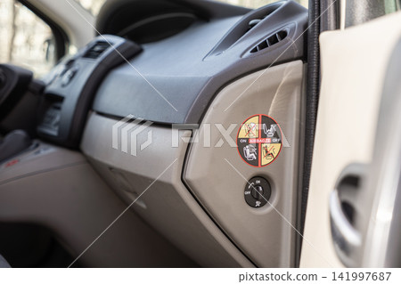 A passenger airbag warning sticker and deactivation switch located inside a modern vehicle cockpit, highlighting essential automotive safety protocols for secure family travel trips A passenger airbag warning sticker and deactivation switch located inside a modern vehicle cockpit, highlighting essential automotive safety protocols for secure family travel trips 141997687