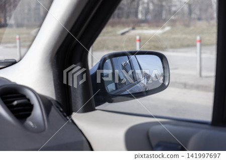 Side mirror reflection of a city building and urban road viewed from inside a parked car, conveying a sense of transition and travel while capturing everyday transit atmosphere Side mirror reflection of a city building and urban road viewed from inside a parked car, conveying a sense of transition and travel while capturing everyday transit atmosphere 141997697