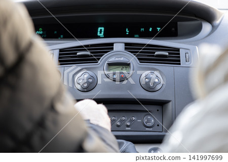 A driver adjusts the climate control settings inside a modern vehicle cabin with a digital speedometer visible while traveling on a road trip to capture the daily navigation experience 141997699