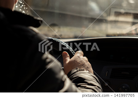 A person grips the black steering wheel of a car on a bright sunny day, conveying focus, commuting, travel, and the personal experience of driving within a busy urban setting 141997705