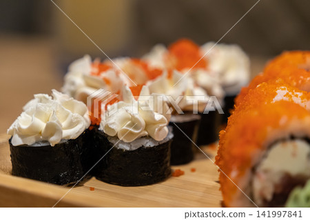 Cream cheese sushi rolls topped with orange fish roe on a wooden serving board for a gourmet japanese dinner experience showcasing fresh ingredients in a stylish restaurant setting Cream cheese sushi rolls topped with orange fish roe on a wooden serving board for a gourmet japanese dinner experience showcasing fresh ingredients in a stylish restaurant setting 141997841