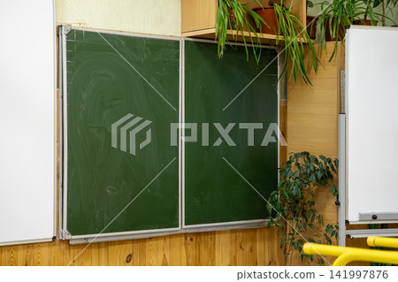 Empty green chalkboard mounted on a classroom wall with potted plants, conveying a sense of academic anticipation and clean learning environment for students in a school setting Empty green chalkboard mounted on a classroom wall with potted plants, conveying a sense of academic anticipation and clean learning environment for students in a school setting 141997876