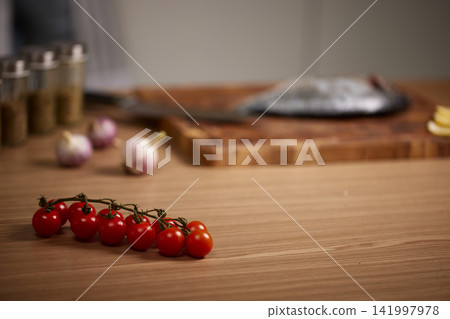 Cherry tomatoes, garlic, and whole fish on cutting board, ready for a healthy meal preparation in kitchen Cherry tomatoes, garlic, and whole fish on cutting board, ready for a healthy meal preparation in kitchen 141997978