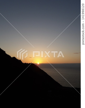 夕陽西下，落日緩緩沉入山脈的地平線。 141998120